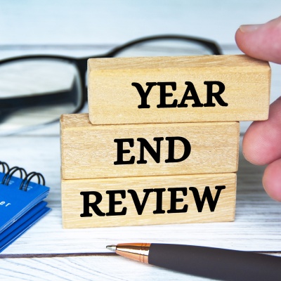 Drei Bauklötze mit den Worten Year End Review, auf Deutsch: Steuererklärung, liegen auf Papieren neben einem Kugelschreiber und einer Brille.